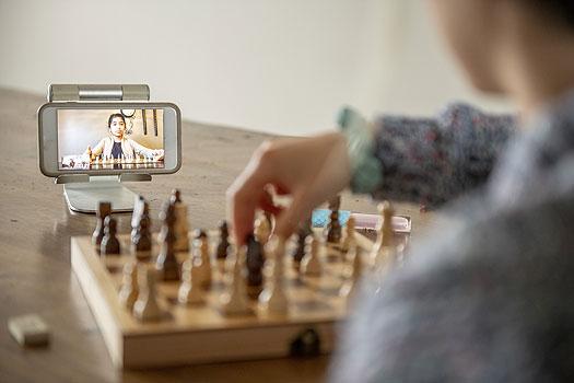 close up image of woman playing chess with a friend who is participating in a video chat