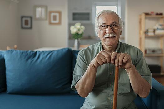 Senior man sitting on sofa leaning forward on his wooden cane