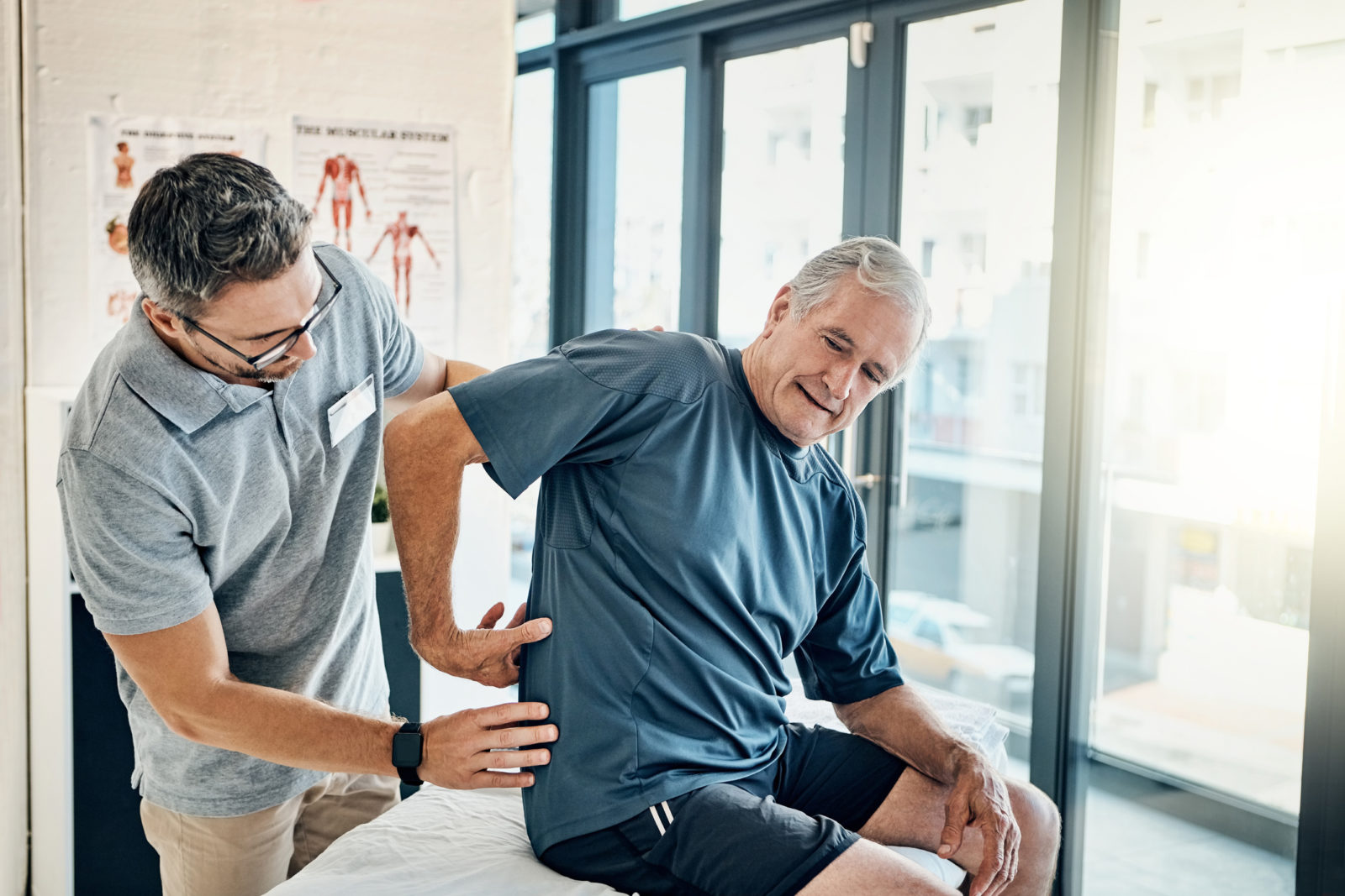 physical therapist helping senior man with back pain at rehab center