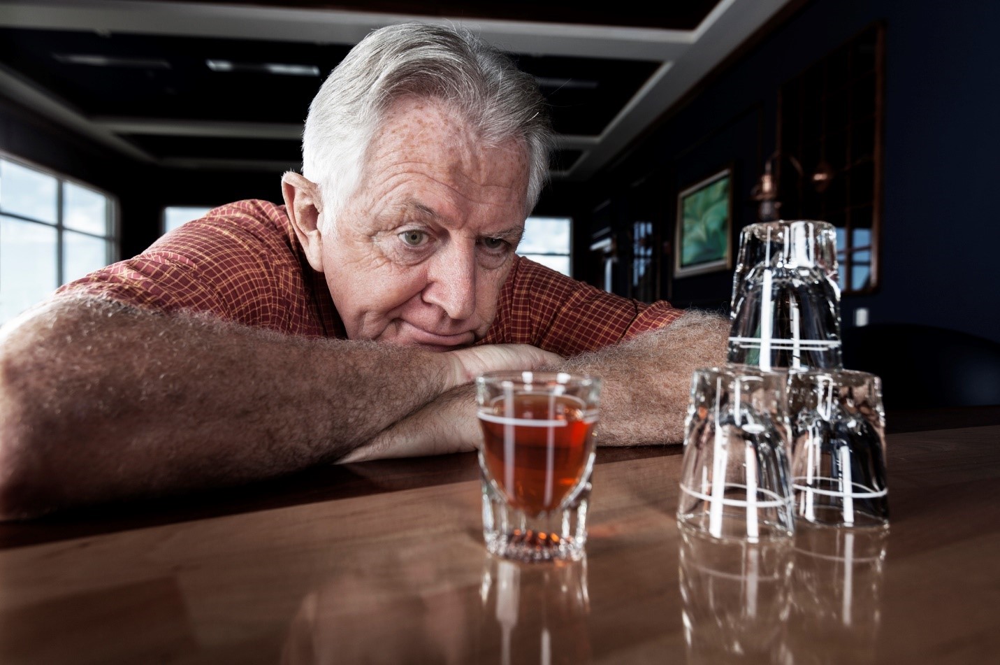 Senior man sitting at bar in pub looking at shot glass with alcohol