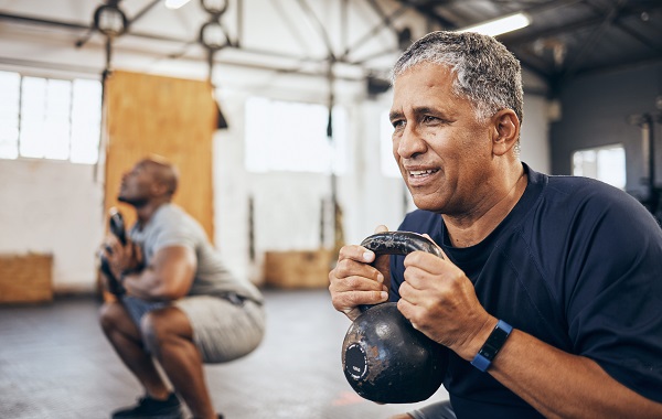 senior man exercise with personal trainer at the gym squat with kettlebell equipment for strength.